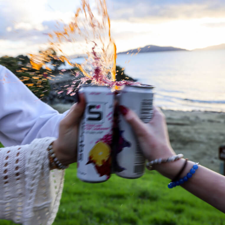 Cheersing cans of Squared at sunset with liquid splashing out the top