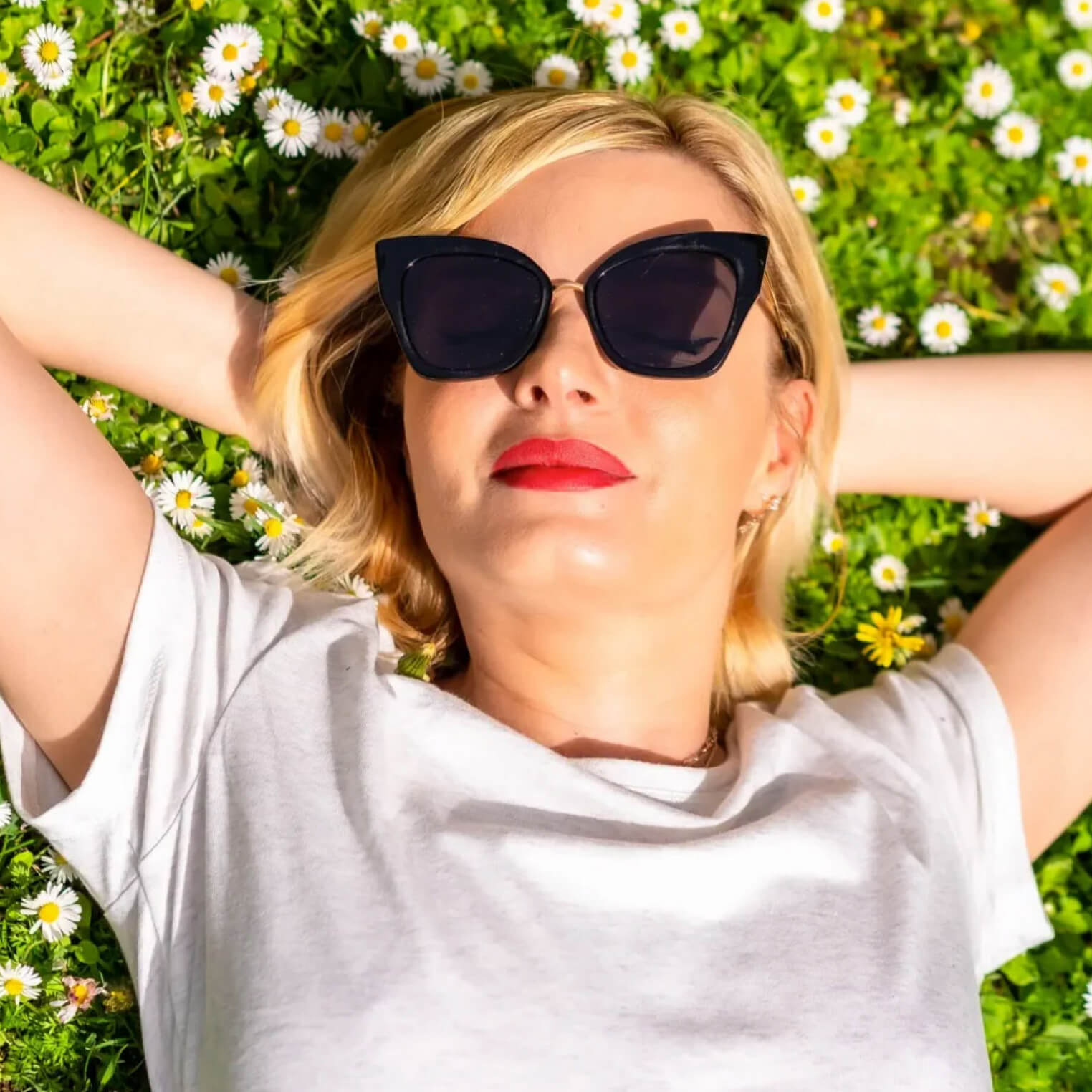 Young woman with blonde hair and stylish sunglasses relaxing in a bed of flowers